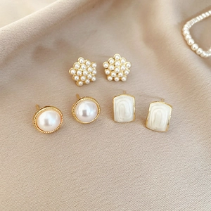 Detailed macro view of gold-plated pearl stud earring set on beige silk fabric