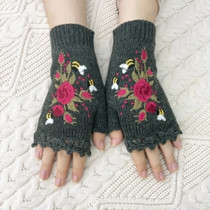Detail shot of dark green knitted fingerless gloves with red rose and bee embroidery