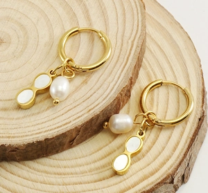 Detail of gold geometric earrings with pearl and peanut charms on wood slice