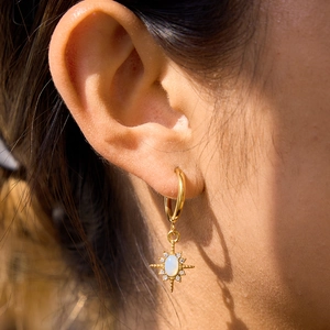 Gold starburst earrings with white opal center and sparkling crystals on female model