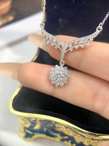 Close-up of silver fish tail sunflower moissanite pendant necklace on finger in blue box