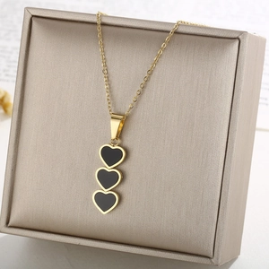 Detail of a gold necklace featuring three black heart pendants in a beige jewelry box