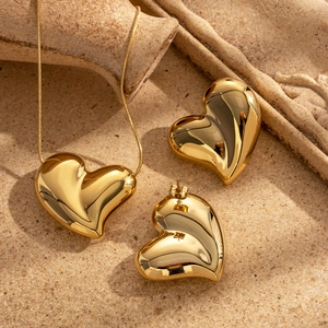Polished gold heart jewelry set with necklace and stud earrings on a textured stone surface