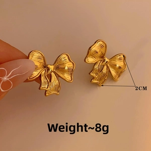Detail shot of golden bow earrings showing 2CM size and brushed metal texture
