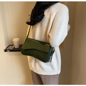 Detail of dark green matte leather shoulder bag with gold buckle on white jacket
