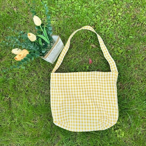 Flat lay of yellow and white checkered canvas tote bag on green grass with tulips