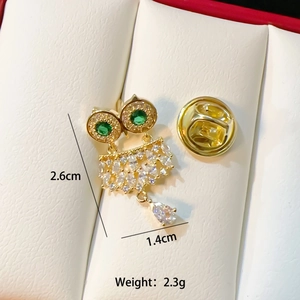 Golden owl brooch with green and clear crystals on a white leather cushion