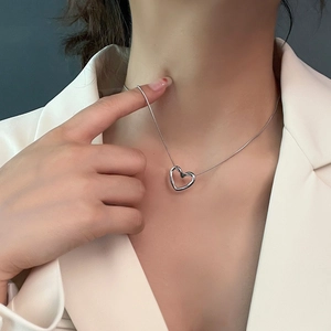 Minimalist silver twisted heart pendant necklace on a model wearing a beige blazer