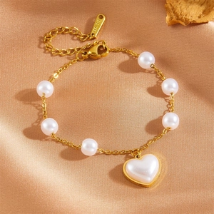 Détail du bracelet perles avec pendentif cœur en acier doré 18K sur fond de soie