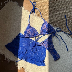 Détail à plat d'un ensemble bikini 3 pièces en dentelle bleue avec une jupe fleurie assortie