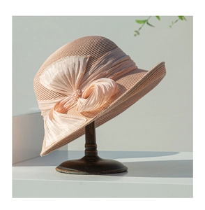 Détail d'un chapeau en paille rose avec un grand nœud et perle sur un support en bois