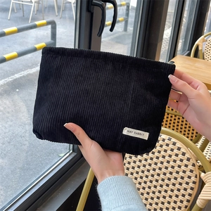 Detail of black corduroy makeup bag held by hand, showing textured fabric and label