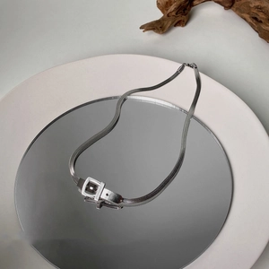 Silver snake chain necklace with buckle pendant on a minimalist ceramic plate