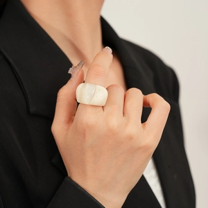 Macro detail of a wide cream resin ring with marble texture worn on the finger