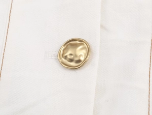 Vue macro détaillée du tissu blanc avec un bouton métallique doré de forme irrégulière