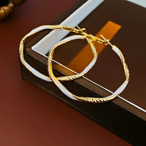 Detail of irregular round gold and white enamel hoop earrings on a dark jewelry box