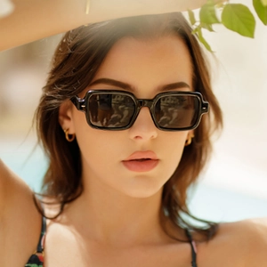 Close-up of black rectangular sunglasses worn by a model in soft outdoor natural light