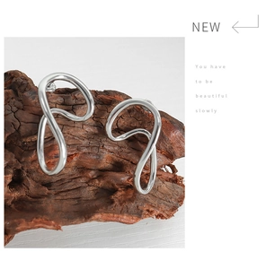 Detailed close-up of twisted silver geometric earrings on a natural wood surface