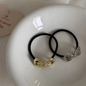 Detailed view of two metallic bow hair ties in gold and silver finish on a ceramic plate
