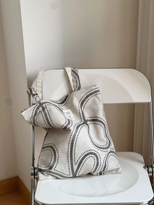 Minimalist canvas tote bag with black geometric print hanging on a white folding chair