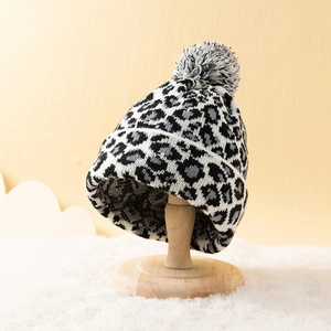 Leopard print knitted beanie for women with large pom-pom detail on a wooden display stand