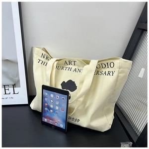 Detail shot of a large canvas tote bag with NK ART STUDIO print and iPad for size scale