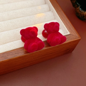 Close-up of red flocked bear stud earrings in a wooden beige velvet jewelry box