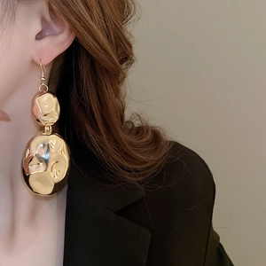 Detail of elegant gold crumpled earrings with high-shine finish on model