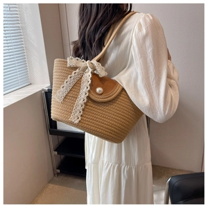 Straw bag featuring a brown leather flap, pearl clasp, and decorative lace bow detail