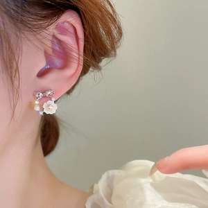 Detail showing crystal bow and white floral stud earring worn on model's ear