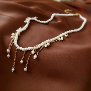 Detail of elegant pearl choker with gold tassel chain on dark silk fabric