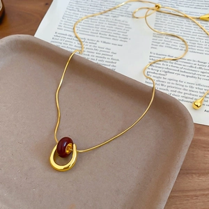 Detail of gold U-shaped pendant necklace with reddish-brown bead and adjustable snake chain