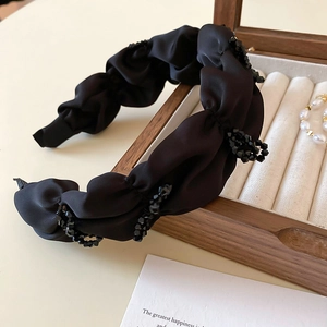 Détail d'un serre-tête en satin noir avec perles de cristal sur un présentoir en velours