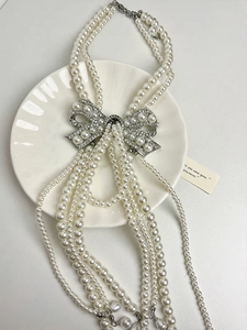 Macro shot of multi-layer pearl necklace with rhinestone bow pendant on white plate