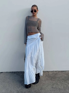 Detail view of stylish layered white maxi skirt paired with grey open-knit top and boots