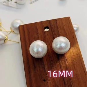 Close-up of 16mm white pearl stud earrings with unique grain texture on wooden display