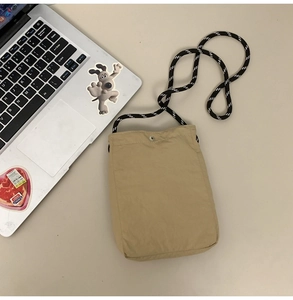 Flat lay of a beige waterproof crossbody phone bag with woven strap and silver metal snap