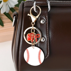 Baseball keychain with red Love heart and bow charms hanging on a leather bag