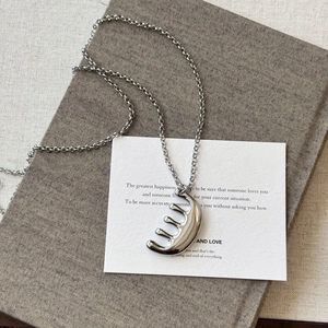 Vue détaillée d'un pendentif peigne argenté sur une chaîne de pull au style minimaliste