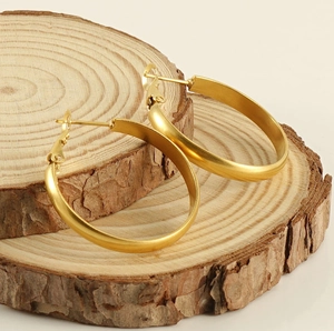 Detailed close-up of matte gold oversized hoop earrings on natural wood slice texture