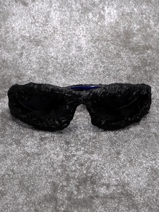 Detail of black avant-garde sunglasses featuring unique lava texture frames on silver glitter