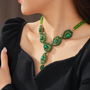 Nahaufnahme einer Vintage-Goldkette mit grünen Tropfensteinen und Blattdesign am Modell