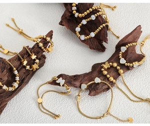 Détail de bracelets perlés plaqués or 18 carats avec breloques papillon et cœur
