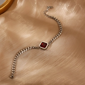Detail eines silbernen Panzerarmbands mit rotem Zirkon auf goldenem Seidenhintergrund
