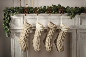 Detail of four beige cable knit Christmas stockings hanging on a white wooden mantel