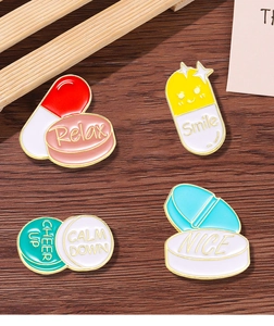 Set of 4 colorful pill enamel pins with Relax and Smile slogans on wood surface