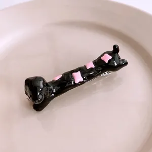 Glossy black resin dachshund hair clip with pink bone accents on a white plate