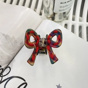 Détail de la pince à cheveux noeud en fil rouge et acrylique sur un fond blanc épuré