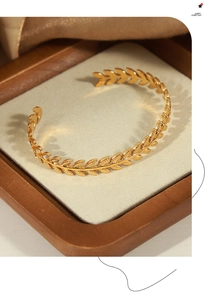 Detailed close-up of golden laurel leaf open bangle on professional display stand