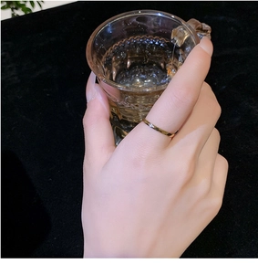 Close-up of a faceted gold titanium steel ring shown on a finger holding a glass